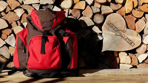 Ein roter Rucksack vor einem Stapel Brennholz